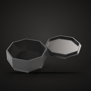 May include: A matte dark gray octagonal container with a matching lid positioned beside it. The container features a hollow interior and a flat base, while the lid is flat with a raised edge that fits the octagonal opening of the base.