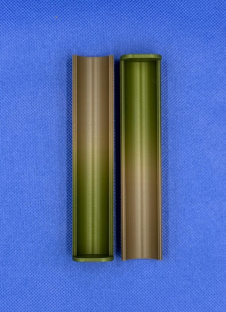May include: Two empty, cylindrical containers made of a brown and green plastic material. The containers are open at one end and closed at the other. They are both standing upright on a blue surface.