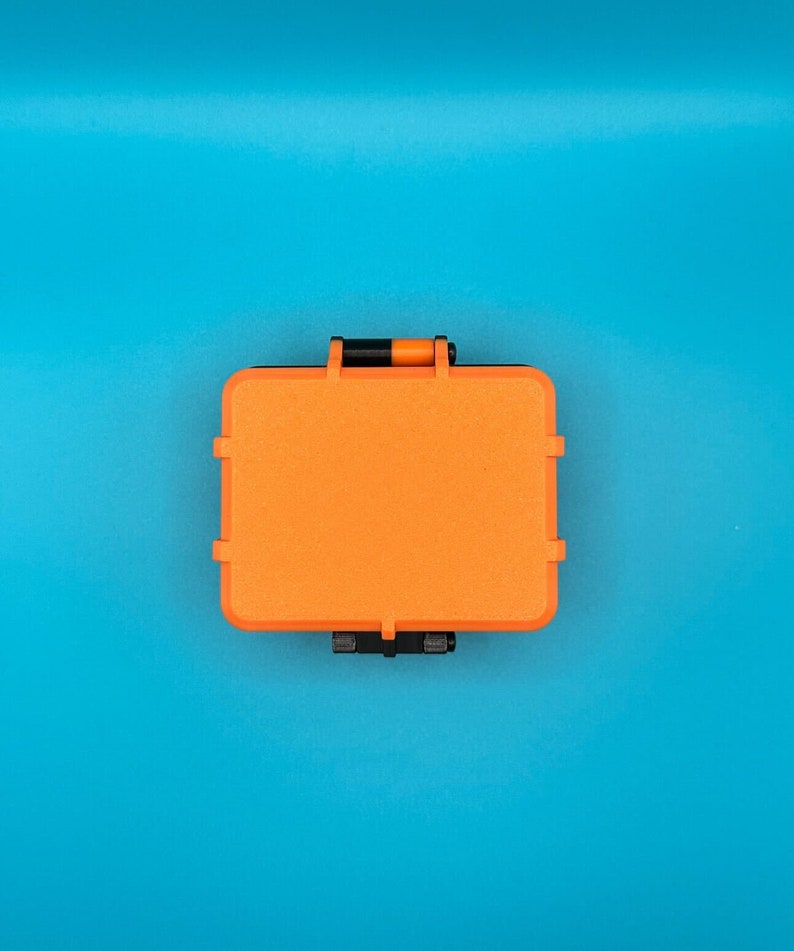 May include: A rectangular, bright orange protective storage case with a textured surface. The case features black hinges and a black latch mechanism on the top and bottom edges, designed for secure closure and durability in various environments.