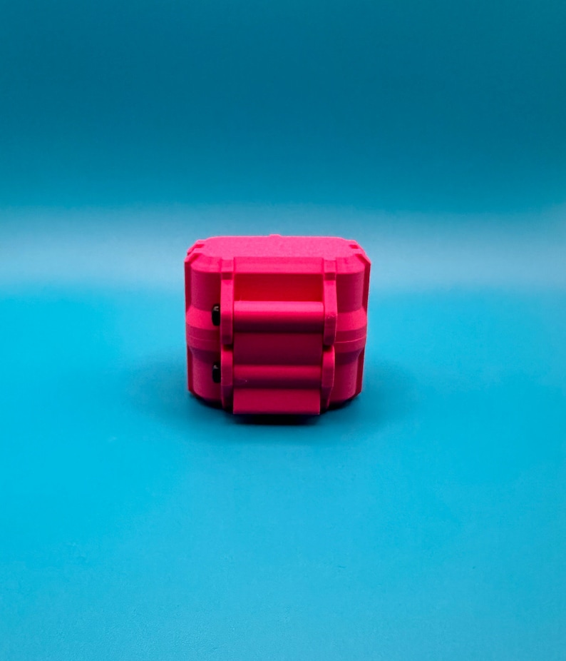 May include: A bright pink, rectangular, hard-shell storage case with a textured surface. The case features a prominent central latch mechanism with two small black circular accents on the side, designed for secure closure and protection.