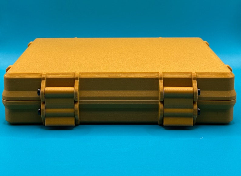 May include: A rectangular, mustard-yellow storage case with a textured, matte finish. The case features a hinged design with two prominent front latches secured by small black pins, providing a sturdy and secure closure for the container.