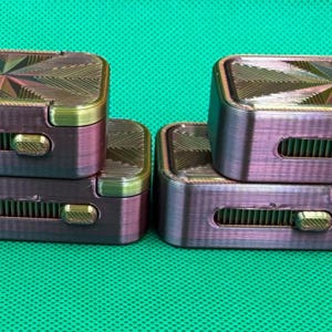 May include: Four rectangular, iridescent purple and gold fidget sliders stacked in two pairs. Each slider features a textured, starburst-patterned top surface and a horizontal side slot containing a sliding gold-coloured metal toggle mechanism.