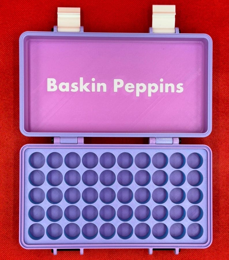 May include: A purple plastic case with a hinged lid and a label that reads "Baskin Peppins". The case has 36 round compartments.