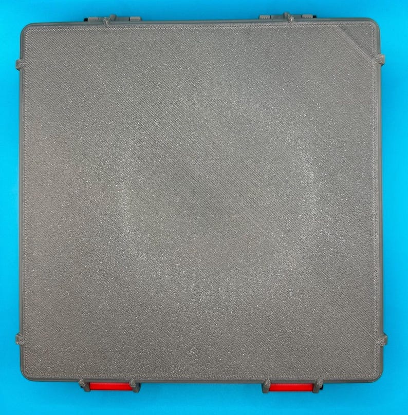 May include: A gray plastic storage box with a textured surface and red accents on the edges.