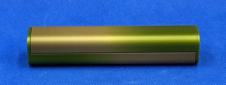 May include: A cylindrical, metallic container with a gradient finish, transitioning from a light gold to a dark green color.