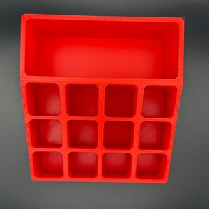 May include: A red plastic organizer with 12 compartments. The organizer has a rectangular shape and is made of a smooth, glossy plastic.