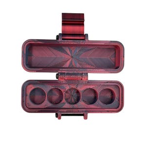 Puede incluir: Un estuche de almacenamiento rectangular con bisagra y acabado jaspeado en rojo y negro. El interior de la base contiene cinco compartimentos circulares, mientras que la tapa superior es hueca con un patr&oacute;n geom&eacute;trico texturizado.