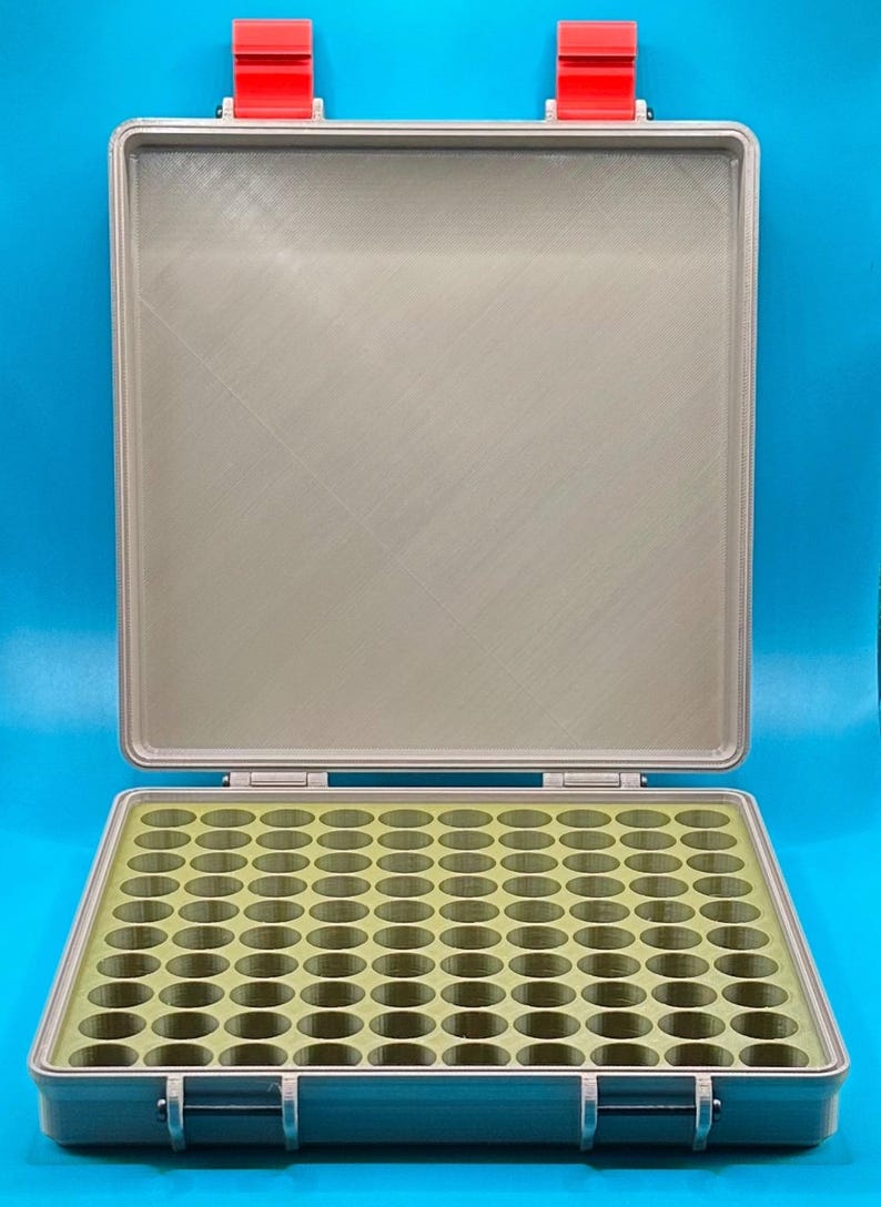 May include: A gray plastic storage case with a hinged lid and red latches. The case has a green foam insert with 100 round compartments.