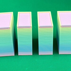 May include: Four rectangular containers with lids, arranged in a row. Each container features a gradient finish transitioning from light yellow at the top to light blue and pink at the base. The lids are a solid light purple color.