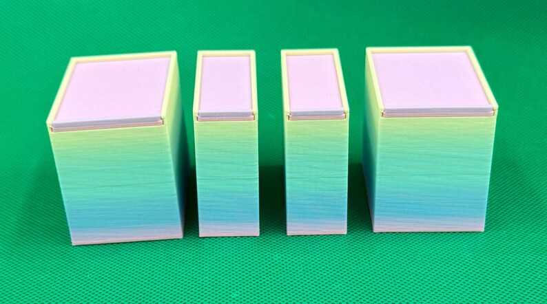 May include: Four rectangular containers with lids, arranged in a row. Each container features a gradient finish transitioning from light yellow at the top to light blue and pink at the base. The lids are a solid light purple color.