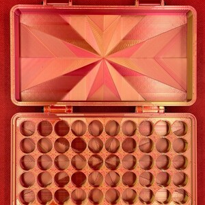May include: A red plastic storage box with a hinged lid. The box has 36 round compartments for storing small items.