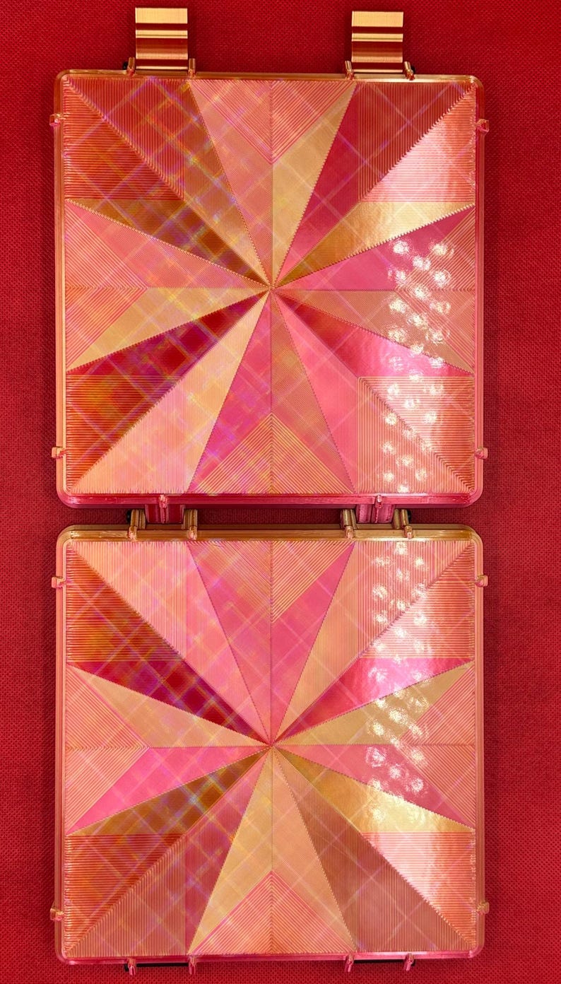 May include: Two square-shaped, pink and gold, decorative tiles with a geometric pattern. The tiles are made of a shiny, iridescent material.