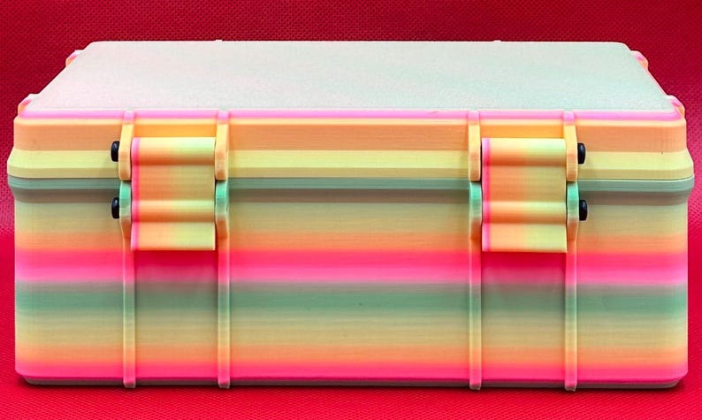Puede incluir: Una caja de almacenamiento de pl&aacute;stico con colores de arco&iacute;ris, con dos cierres y una tapa texturizada. La caja tiene un dise&ntilde;o de rayas multicolores con tonos rosas, naranjas, amarillos, verdes y azules.
