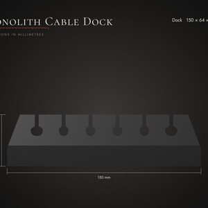 Op de afbeelding: Een donkergrijze rechthoekige Monolith Cable Dock met zes ronde kabelsleuven langs de bovenrand. De tekst luidt Monolith Cable Dock en Dock 150 x 64 x 40 mm. De afmetingen zijn aangegeven als 150 mm in lengte en 40 mm in hoogte.