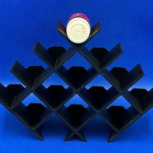 Puede incluir: Un estante de almacenamiento negro en forma de pir&aacute;mide con m&uacute;ltiples compartimentos en forma de diamante. Una botella peque&ntilde;a y redonda con tapa blanca y etiqueta rosa descansa en la ranura superior del estante, dise&ntilde;ado para objetos cil&iacute;ndricos.