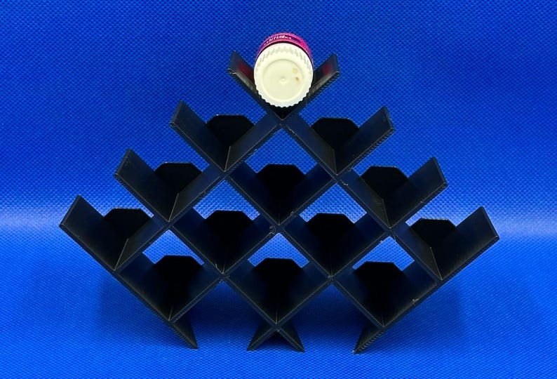 Puede incluir: Un estante de almacenamiento negro en forma de pir&aacute;mide con m&uacute;ltiples compartimentos en forma de diamante. Una botella peque&ntilde;a y redonda con tapa blanca y etiqueta rosa descansa en la ranura superior del estante, dise&ntilde;ado para objetos cil&iacute;ndricos.
