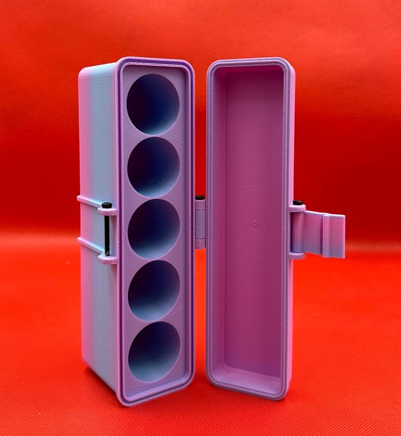 May include: A rectangular, light purple and blue gradient storage case with a hinged lid. The interior features a vertical insert with five circular cutouts for holding cylindrical items, secured by a small black metal hinge pin on the side.
