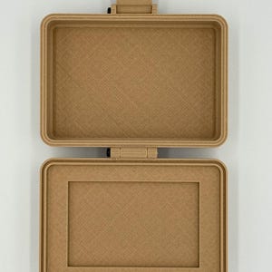 Puede incluir: Una caja rectangular abierta de color marr&oacute;n claro con una superficie texturizada. La caja tiene una tapa con bisagras y un cierre de pestillo. El interior de la caja tambi&eacute;n es marr&oacute;n claro y rectangular, con un borde elevado.