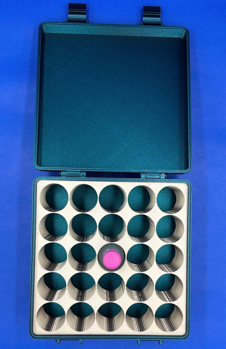 May include: A teal green storage case with a lid, containing 25 round compartments. One compartment has a pink and gray lid.