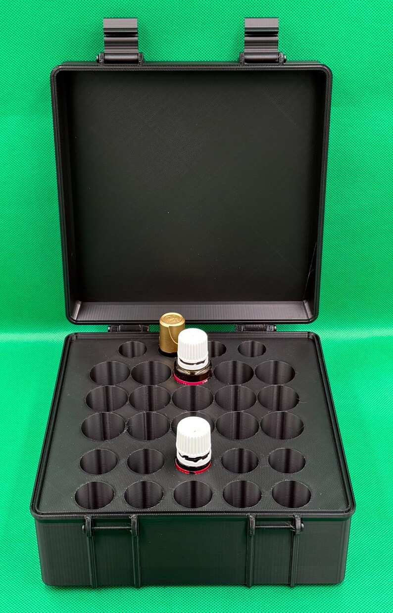 May include: A black rectangular storage case with a hinged lid, featuring a custom interior insert with twenty-five circular cutouts. Two small glass bottles with white screw-on caps are placed within the organised grid of the storage box.