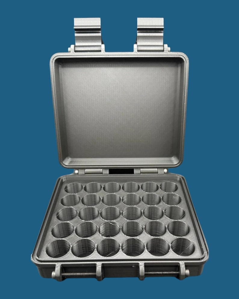 May include: A dark gray, rectangular, hard-shell storage case with an open lid. The interior base features a grid of twenty-five circular, cylindrical compartments arranged in a five-by-five pattern, designed for holding small, round items.