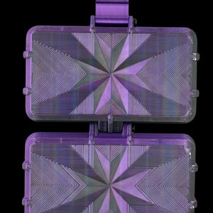 K&ouml;nnte beinhalten: Ein violettes, 3D-gedrucktes rechteckiges Geh&auml;use mit einem geometrischen Sternmuster auf der Vorderseite. Das Geh&auml;use besteht aus zwei identischen, aufklappbaren Abschnitten, die durch ein zentrales vertikales Scharnier verbunden sind.
