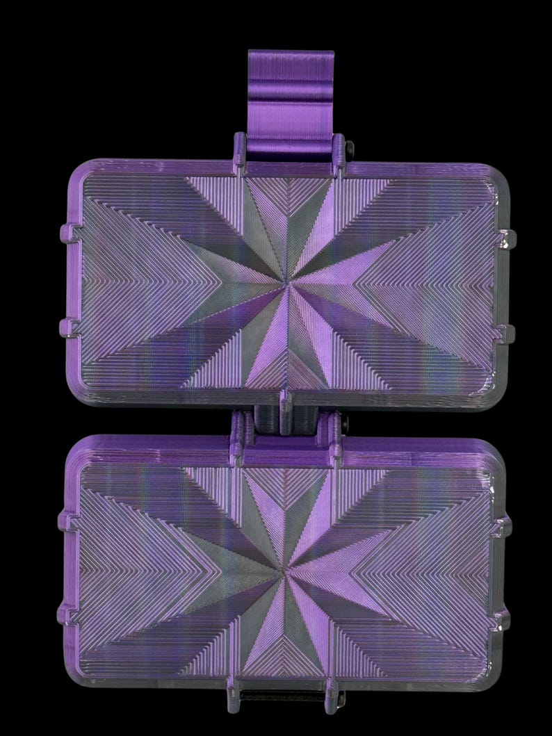 K&ouml;nnte beinhalten: Ein violettes, 3D-gedrucktes rechteckiges Geh&auml;use mit einem geometrischen Sternmuster auf der Vorderseite. Das Geh&auml;use besteht aus zwei identischen, aufklappbaren Abschnitten, die durch ein zentrales vertikales Scharnier verbunden sind.