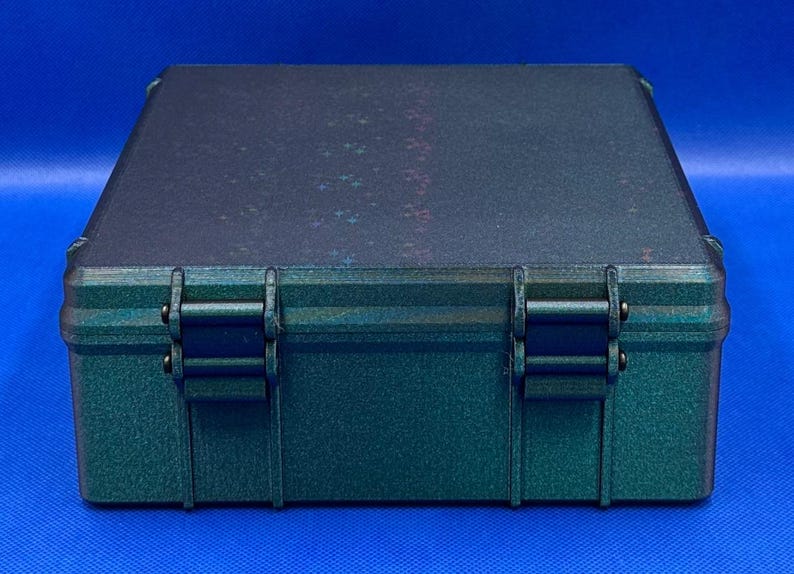 May include: A dark green plastic storage case with two black latches. The case has a textured surface and a iridescent finish.