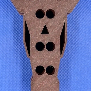 May include: A brown wooden horse head with cut-out eyes, nose, and mouth. The horse head has a textured surface and is a decorative object.