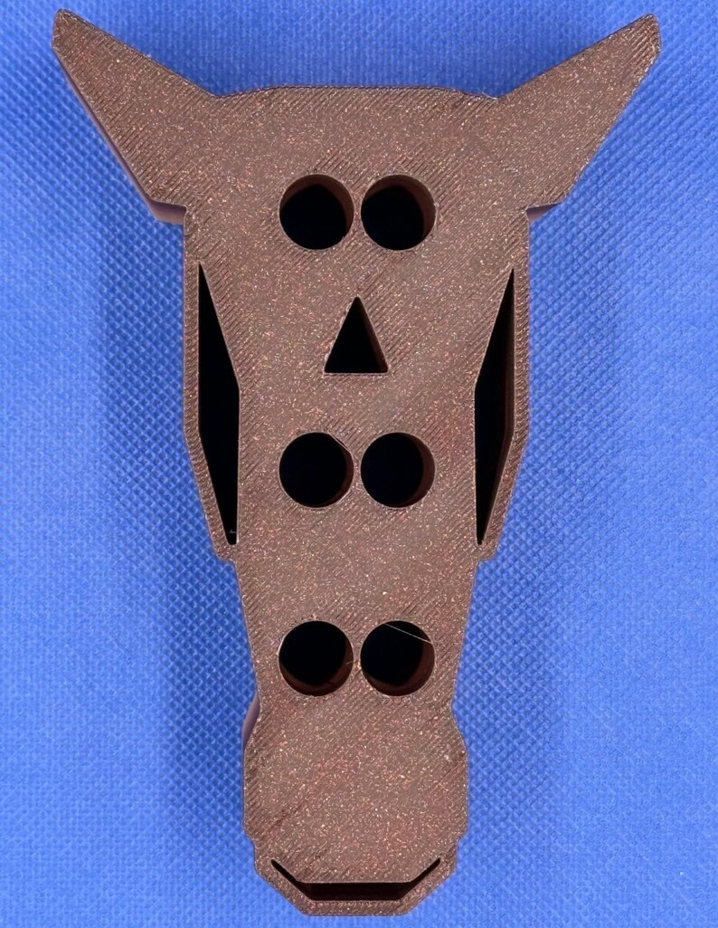 May include: A brown wooden horse head with cut-out eyes, nose, and mouth. The horse head has a textured surface and is a decorative object.