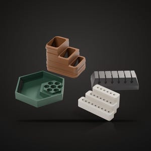 May include: A collection of desk organizers including a brown tiered tray, a green hexagonal tray with a circular insert, a dark gray rectangular block with vertical slots, and a white three-tiered stand with small circular holes.