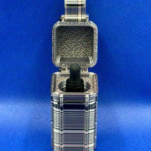 May include: A rectangular, hinged storage case with a black and white striped pattern on the exterior and a textured interior. Inside the case, a black dropper bottle is positioned upright, with the black rubber bulb visible at the top.
