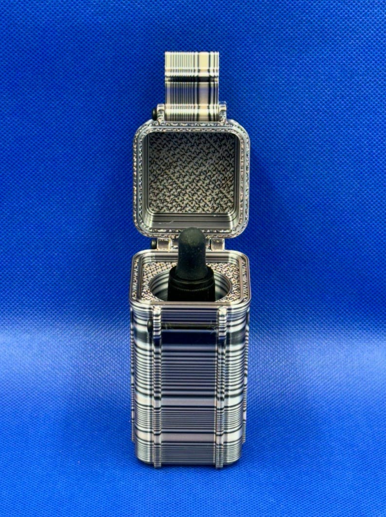 May include: A rectangular, hinged storage case with a black and white striped pattern on the exterior and a textured interior. Inside the case, a black dropper bottle is positioned upright, with the black rubber bulb visible at the top.