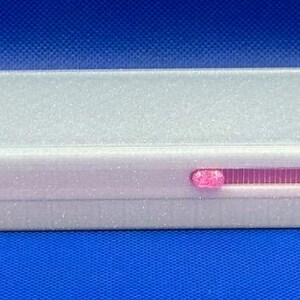 May include: A rectangular white pencil case with a sliding lid and a pink interior. The case features a small pink sliding mechanism on the side and contains a single orange pencil visible in the open compartment on the left side.