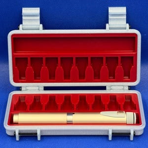 May include: A light gray rectangular storage case with a hinged lid and a bright red interior insert featuring ten molded slots. A single cylindrical gold-colored pen-like tool with a white clip rests horizontally in the bottom section.