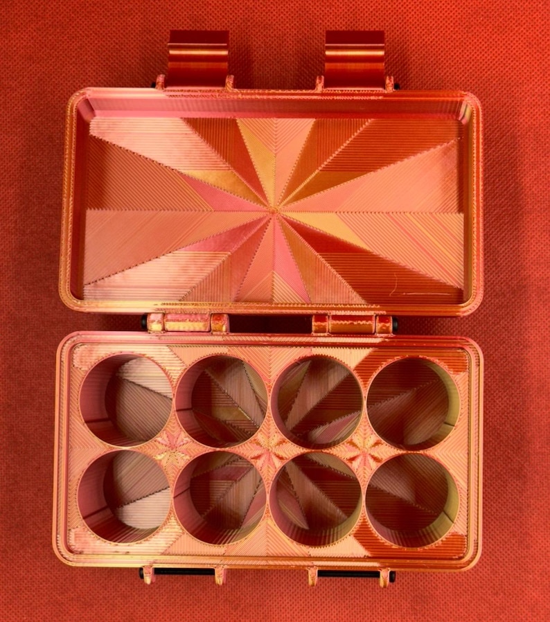 May include: An orange plastic box with a hinged lid and six round compartments. The box has a geometric pattern on the lid and inside the compartments.