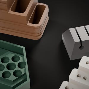 May include: A collection of desk organizers including a brown tiered tray with rectangular compartments, a green hexagonal tray with seven circular holes, a gray block with four vertical slots, and a white tiered stand with hexagonal holes.