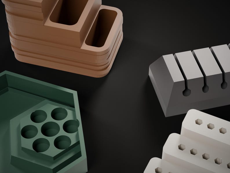 May include: A collection of desk organizers including a brown tiered tray with rectangular compartments, a green hexagonal tray with seven circular holes, a gray block with four vertical slots, and a white tiered stand with hexagonal holes.
