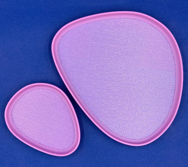 May include: Two pink, oval-shaped trays with a textured surface. The larger tray is slightly larger than the smaller tray.