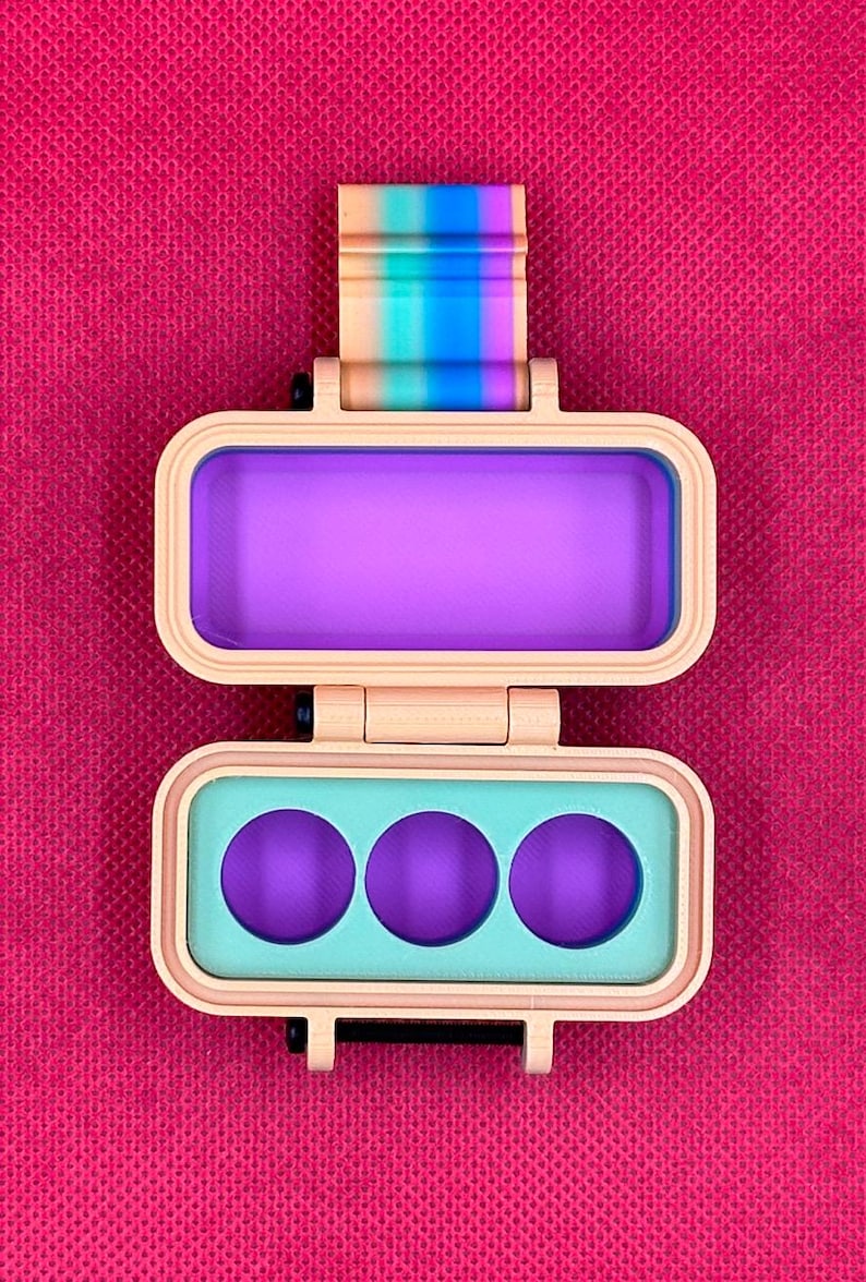 Puede incluir: Una caja rectangular de pl&aacute;stico beige con bisagras y un cierre de rayas arco&iacute;ris. La secci&oacute;n superior presenta un interior rectangular de color morado intenso, mientras que la secci&oacute;n inferior contiene un inserto verde claro con tres aberturas circulares moradas.