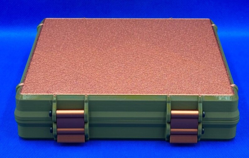 K&ouml;nnte beinhalten: Eine gr&uuml;ne und kupferfarbene Aufbewahrungsbox mit zwei Riegeln. Die Box hat einen strukturierten Deckel.