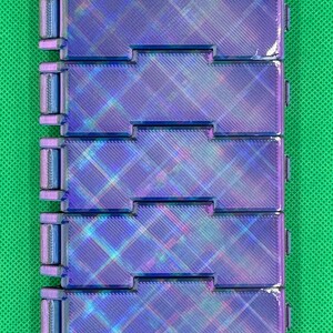 May include: A rectangular, articulated fidget toy composed of seven interconnected, iridescent purple and blue plastic segments. Each segment features a textured, diagonal cross-hatch pattern on its surface, creating a metallic, shifting light effect across the entire linked structure.
