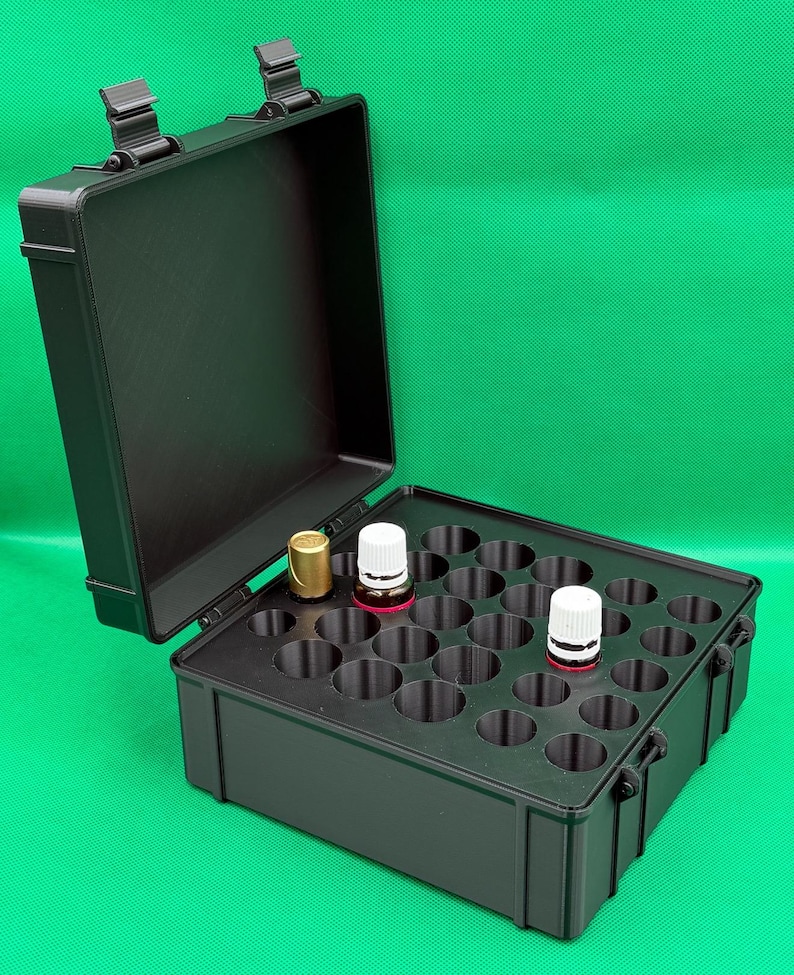 May include: A black rectangular storage case with a hinged lid, featuring a moulded interior insert with twenty-five circular slots. Three small glass bottles with white and gold caps are placed in the slots of the organiser case.
