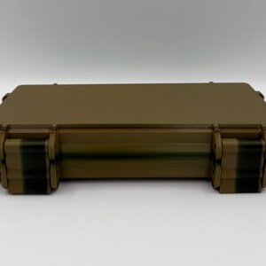 May include: A rectangular, tan-colored hard-shell storage case with a smooth, flat top surface. The case features two prominent, dark-colored locking latches on the front edge, designed to secure the lid firmly to the base of the container.