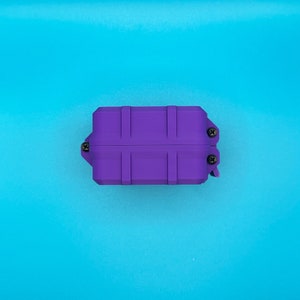 May include: A rectangular purple storage case with a ribbed exterior design. The case features three visible black screws securing the side panels and a hinged closure mechanism on the right side, presented in a solid, uniform color.