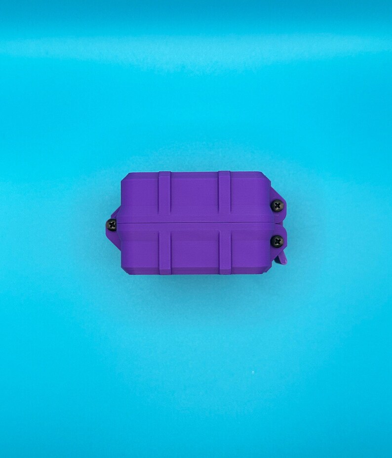 May include: A rectangular purple storage case with a ribbed exterior design. The case features three visible black screws securing the side panels and a hinged closure mechanism on the right side, presented in a solid, uniform color.