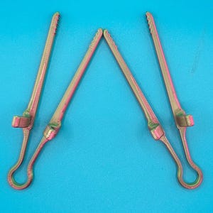 May include: Four long, slender, metallic gold and pink iridescent clips with a textured surface. Each clip features a circular loop at one end, a small perpendicular tab near the base, and a serrated edge along the top length of the arm.