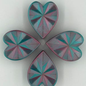 May include: Four heart-shaped objects arranged in a cloverleaf pattern. Each heart features a geometric design with teal, pink, and purple hues. The objects appear to be made of a textured material.