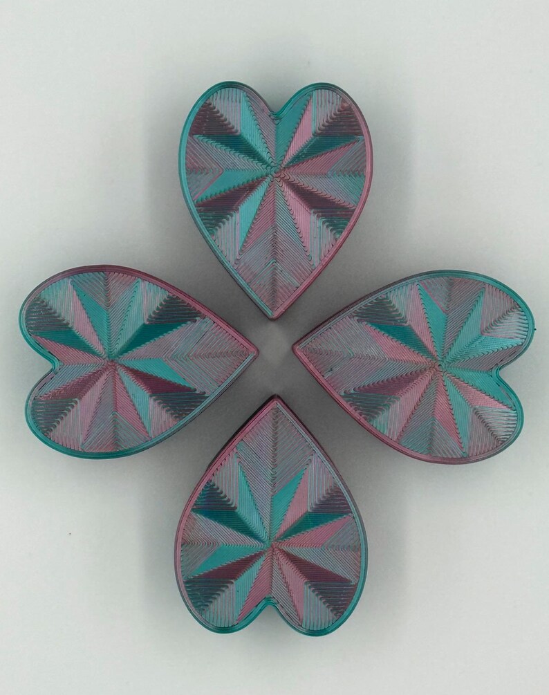 May include: Four heart-shaped objects arranged in a cloverleaf pattern. Each heart features a geometric design with teal, pink, and purple hues. The objects appear to be made of a textured material.