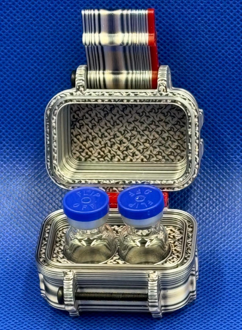 K&ouml;nnte beinhalten: Ein silberfarbenes, rechteckiges, 3D-gedrucktes Aufbewahrungsetui mit Klappdeckel und strukturiertem Innenmuster. Im Inneren befinden sich zwei kleine, durchsichtige Glasfl&auml;schchen mit blauen Kunststoffkappen mit der Aufschrift "FLIP OFF".